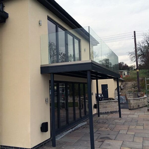 Structural Steel Balconies 5 A contemporary house featuring a walk-on structural steel balcony with clear glass panels, supported by sturdy steel beams, providing an elegant and modern outdoor space above a patio area.