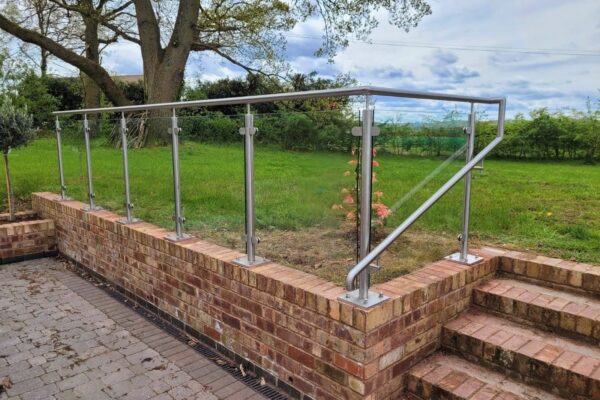 Outdoor stainless steel and glass balustrade installed on a brick patio, featuring sleek metal posts and a handrail, providing a modern and safe barrier while enhancing the aesthetic appeal of the terrace