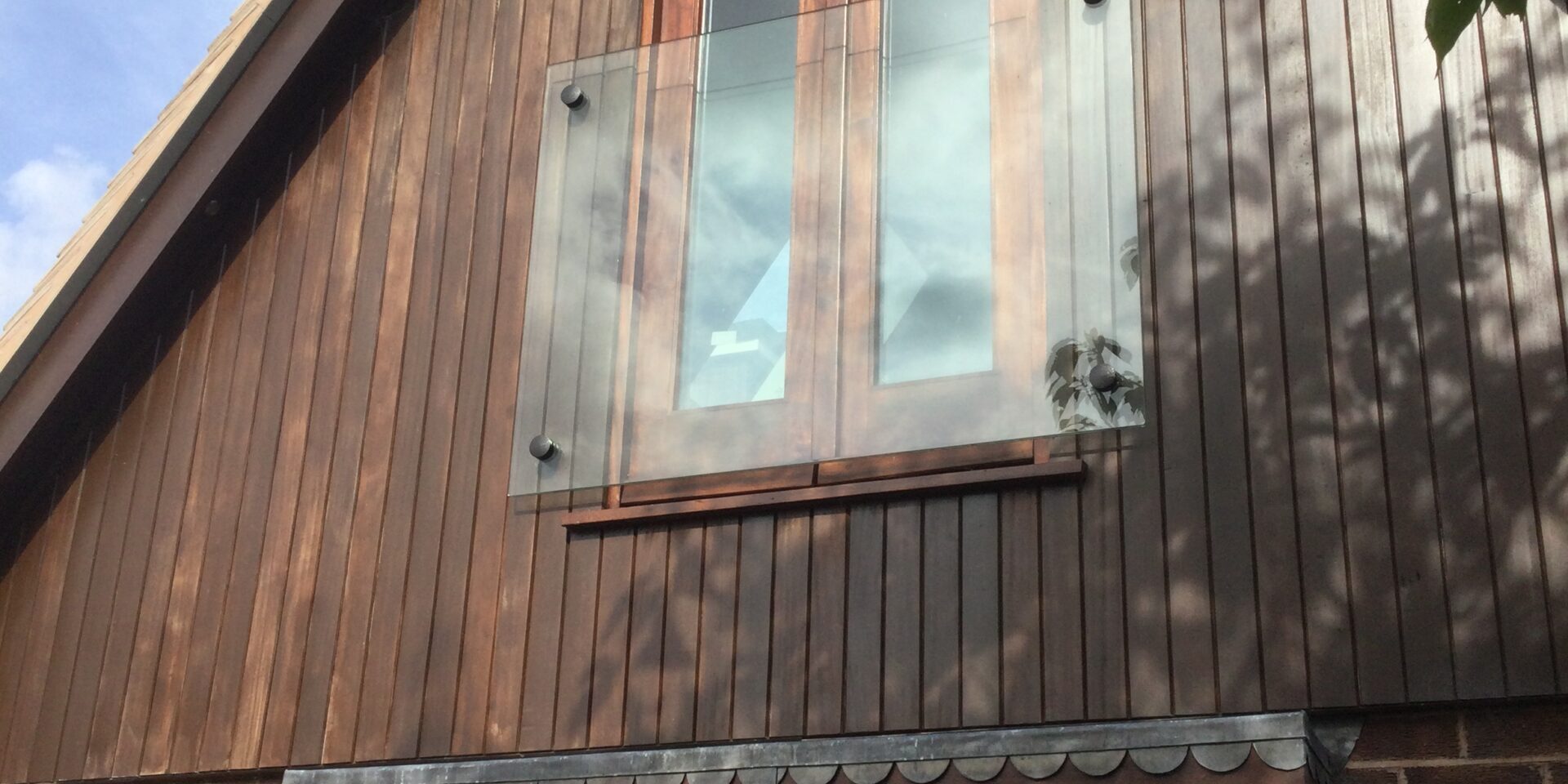 Frameless glass Juliet balcony installed on a modern home, featuring clear toughened safety glass secured with stainless steel adaptors, blending seamlessly with the home's architectural style.