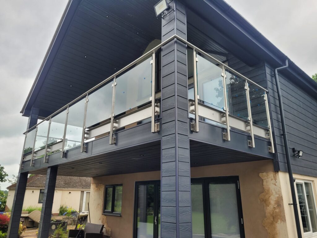A modern two-story house featuring a stainless steel glass balustrade system on the upper balcony, with clear glass panels and sleek stainless steel posts and handrails, enhancing the architectural elegance and providing safety.