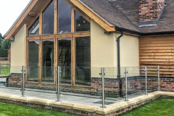 Contemporary house with an outdoor glass balustrade system, featuring stainless steel posts and clear glass panels, enhancing the patio area with a modern and stylish barrier