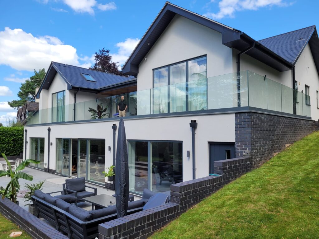 WhatsApp Image 2024-08-08 at 11.18.05_ceafc479 Large frameless glass balustrade surrounding a second-floor terrace, mounted on a base fixed track with a gray powder-coated finish, enhancing the modern exterior of a two-story home