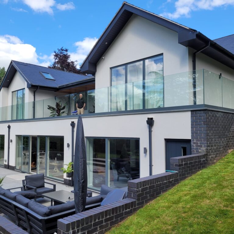 WhatsApp Image 2024-08-08 at 11.18.05_ceafc479 Large frameless glass balustrade surrounding a second-floor terrace, mounted on a base fixed track with a gray powder-coated finish, enhancing the modern exterior of a two-story home