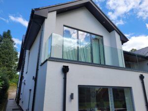 Side view of a modern house featuring a frameless glass balustrade with a gray powder-coated base fixed track, providing safety and style.
