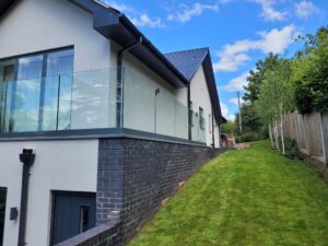 Elegant frameless glass balustrade with a gray powder-coated base fixed track, wrapping around a spacious balcony on a modern home.