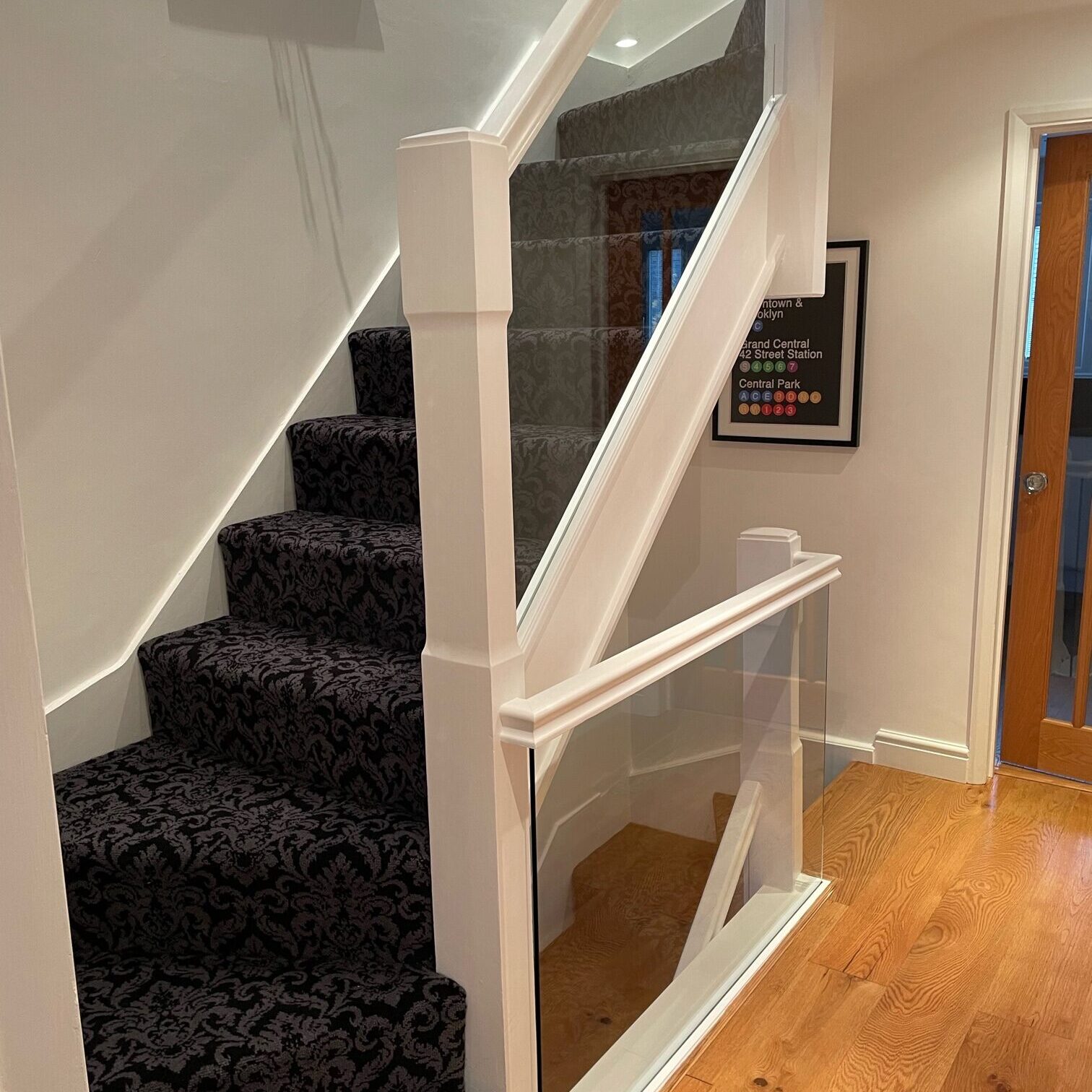 Glass Staircase Banisters 4 Modern staircase with clamps, featuring clear glass panels bolted onto the top of the stringer and underneath the wood handrail, providing a sleek and modern barrier on the side of the staircase.