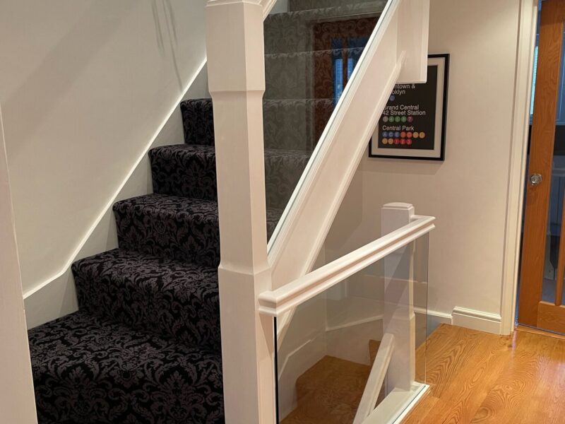 image3 Modern staircase with clamps, featuring clear glass panels bolted onto the top of the stringer and underneath the wood handrail, providing a sleek and modern barrier on the side of the staircase.