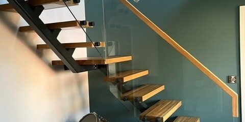 Modern floating glass steel staircase with single spine steel structure, oak timber treads, and seamless glass balustrades, creating a minimalist yet striking focal point in a contemporary home.