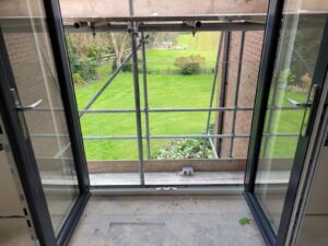 Interior view through open doors onto the Frameless Boss Juliet Balcony, offering an unobstructed view of a lush garden.