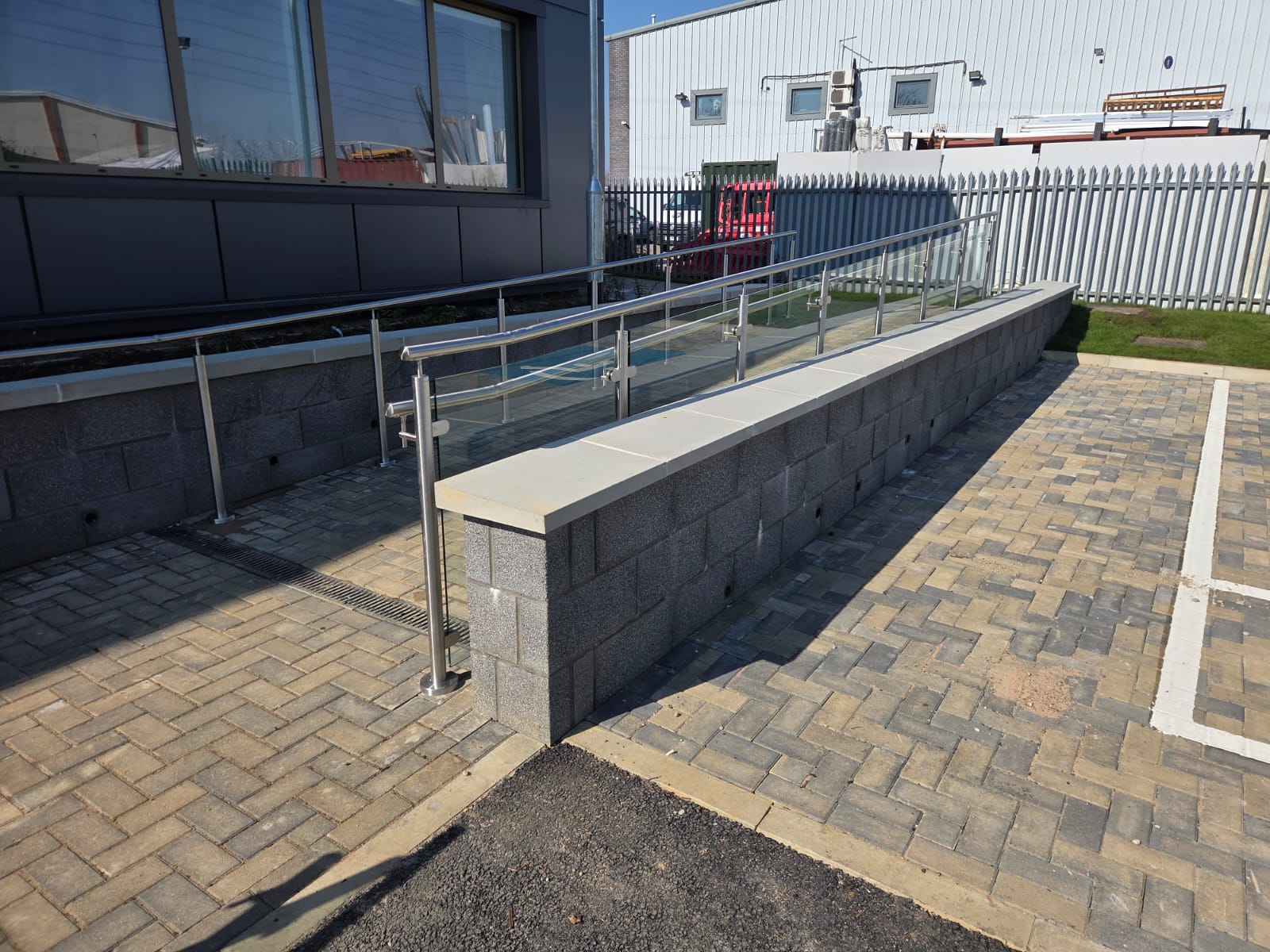 External glass balustrade ramp showing slope transition and paving detail at Northampton mortuary