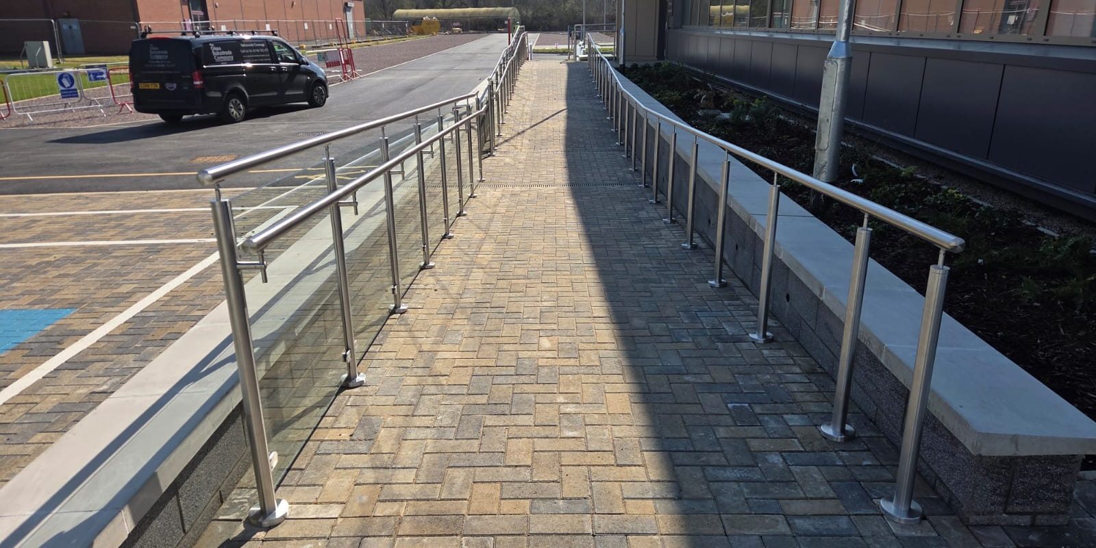 Long run of glass balustrade ramp with stainless steel handrail and posts alongside commercial building in Northampton