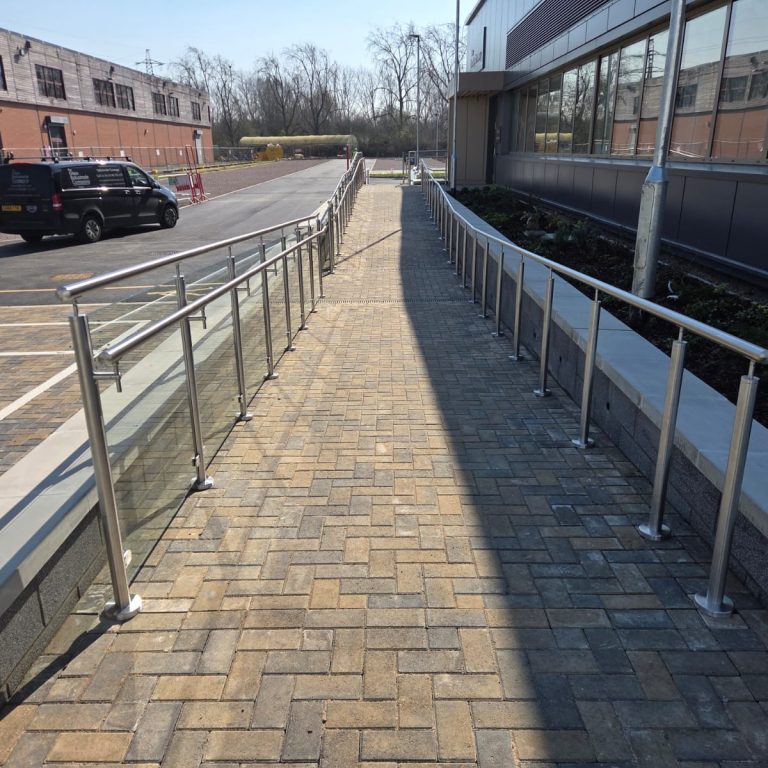 Long run of glass balustrade ramp with stainless steel handrail and posts alongside commercial building in Northampton