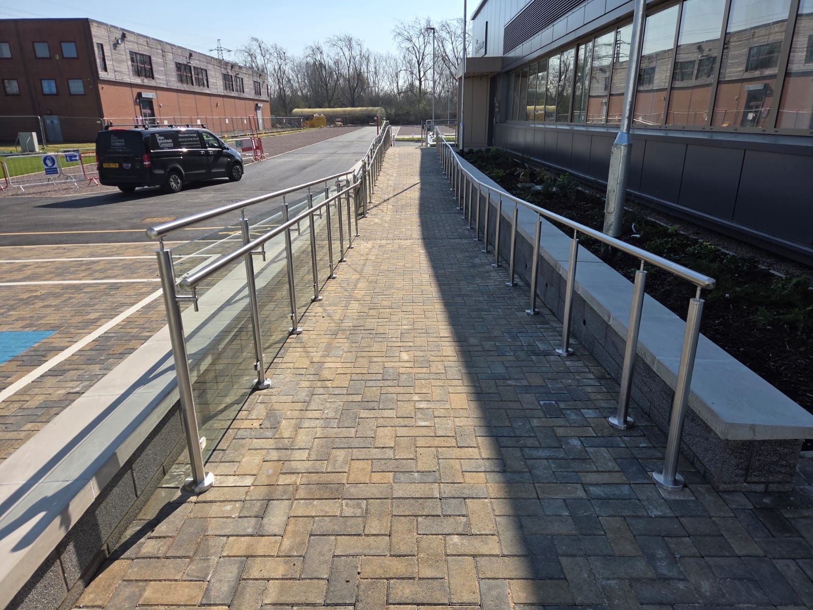 Long run of glass balustrade ramp with stainless steel handrail and posts alongside commercial building in Northampton